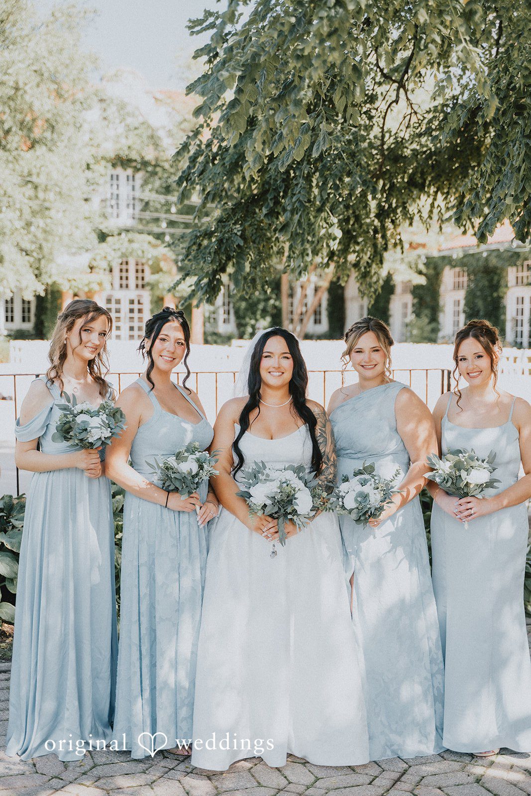 Carly + Dillon A bride posing with her bridesmaids in matching light blue dresses holding bouquets.