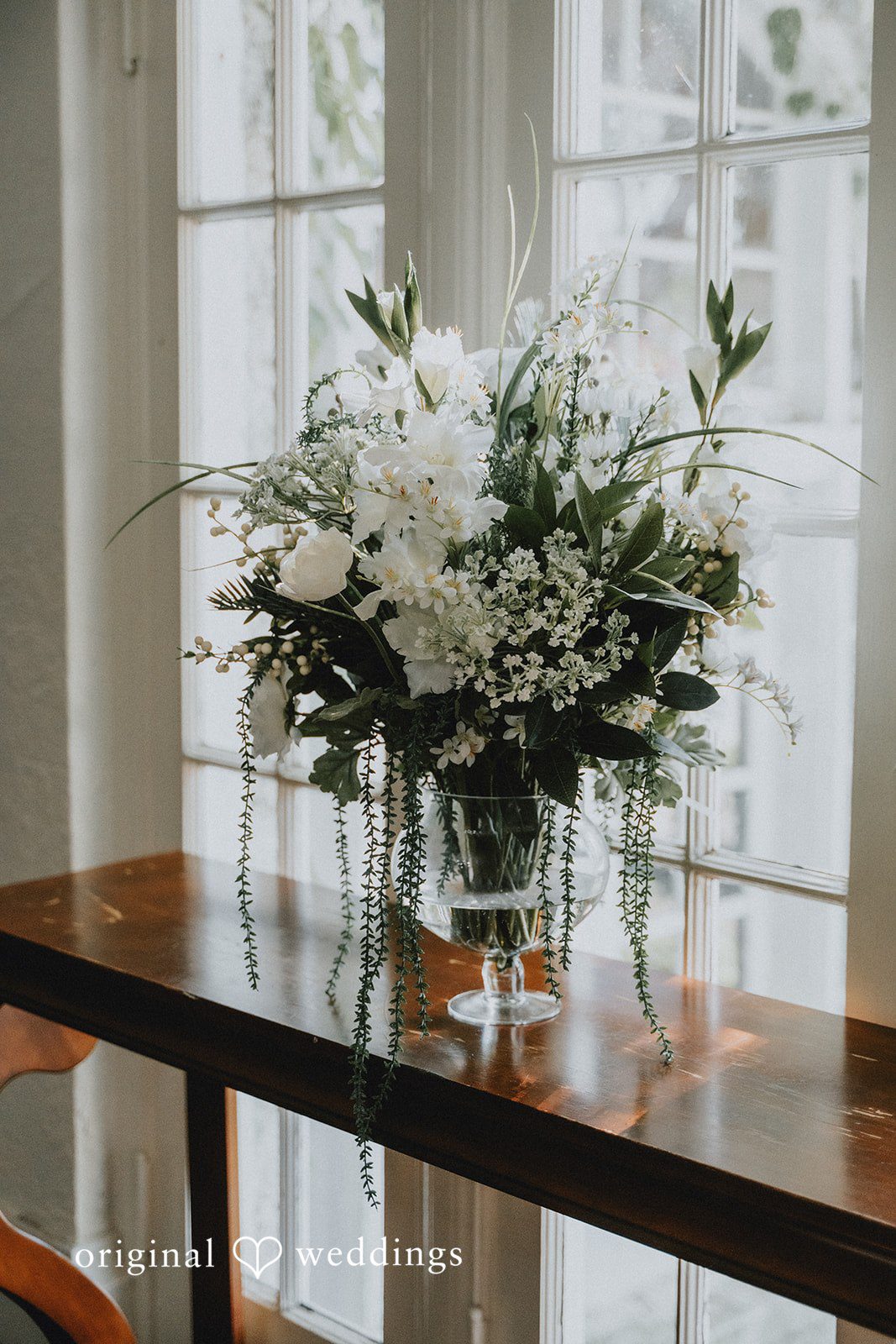 Carly + Dillon A floral arrangement featuring white flowers and green foliage sitting on a wooden surface.