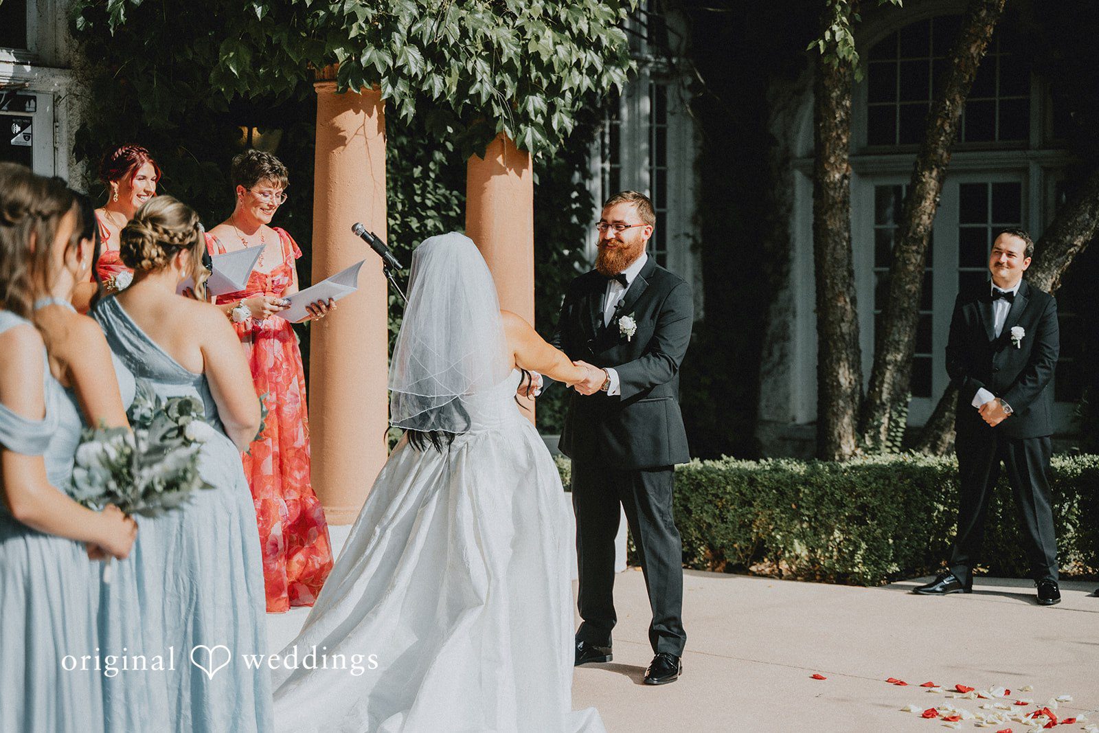 Carly + Dillon A bride and groom holding hands during their wedding ceremony with bridesmaids standing nearby.