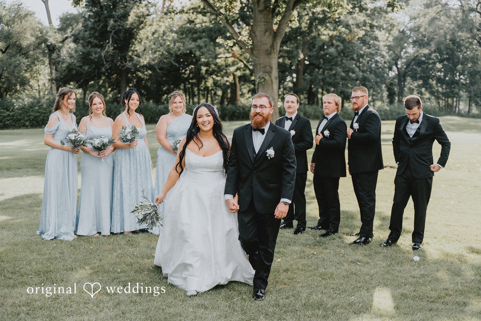 Carly + Dillon A bride and groom walking across a lawn flanked by their wedding party.