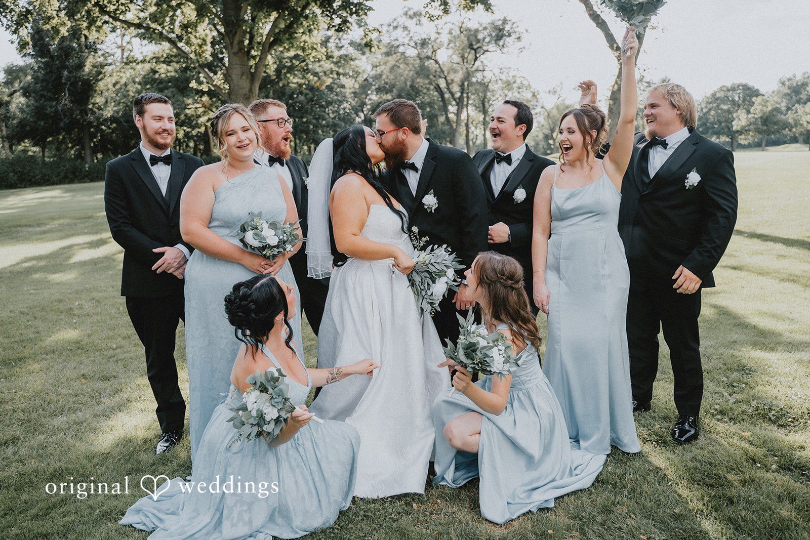 Carly + Dillon A wedding party gathered together on a lawn for a group portrait session.