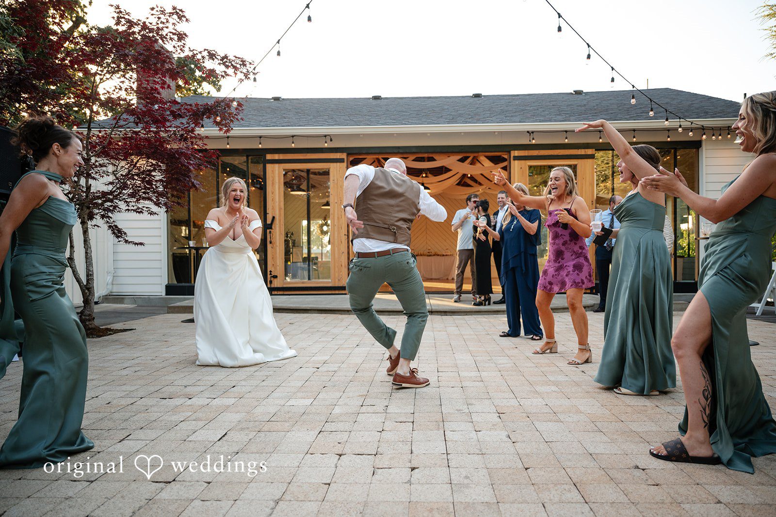 Victoria + Skyler Groom dancing enthusiastically on a patio while guests watch and cheer.