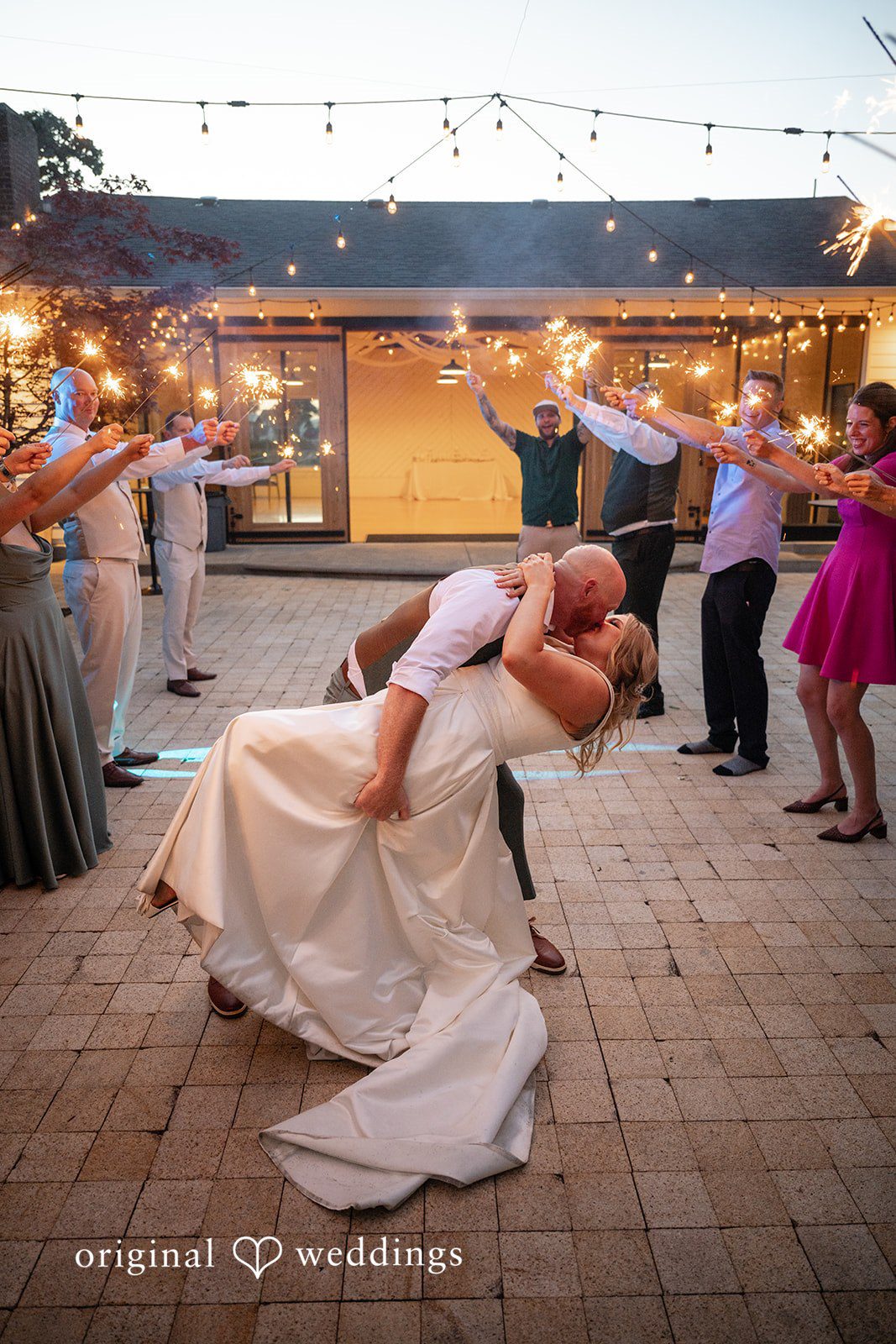 Victoria + Skyler Groom dipping the bride during a dance on a paved patio under string lights.
