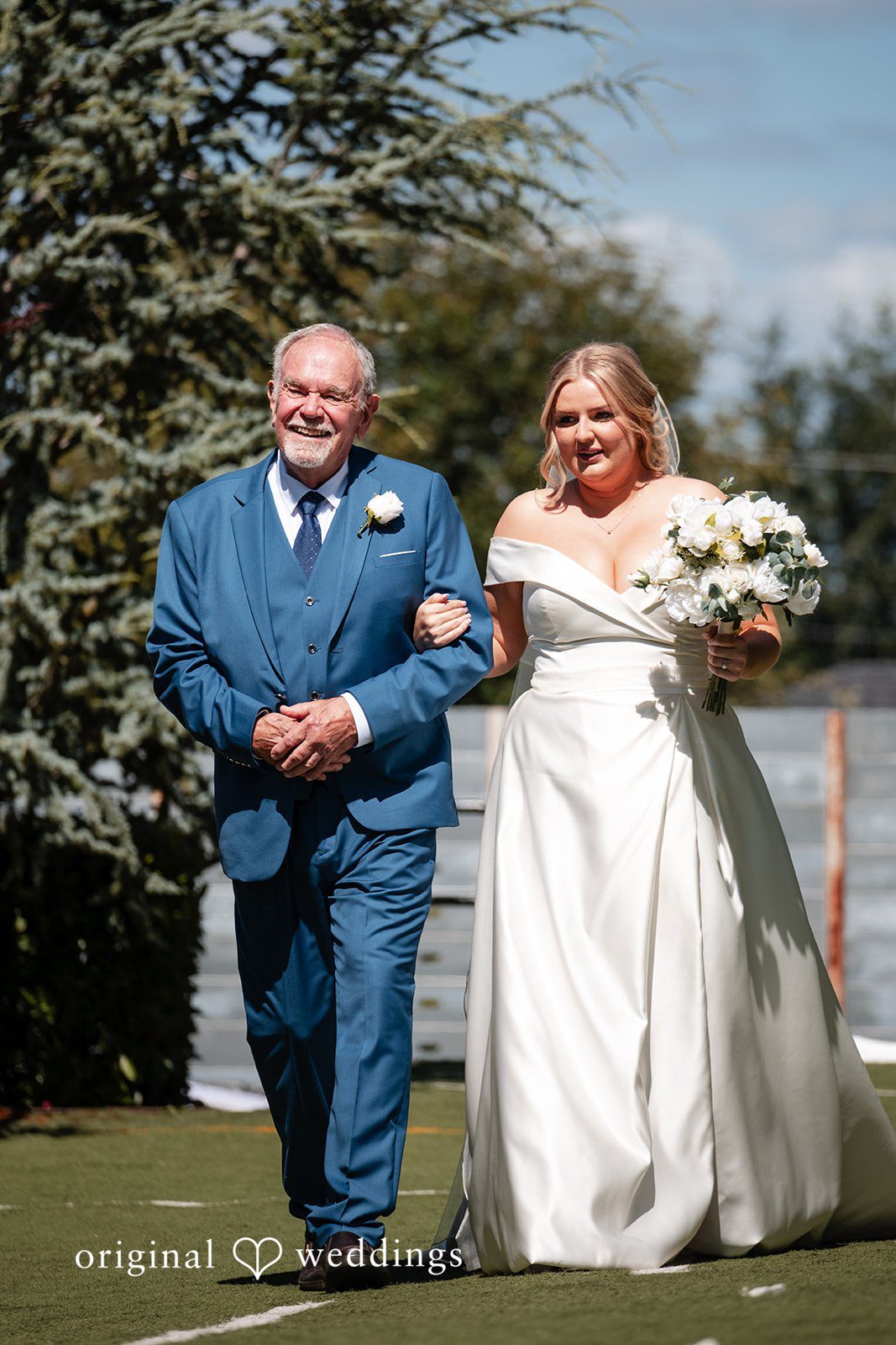 Victoria + Skyler Bride in a white gown walking down the aisle with a man in a blue suit.