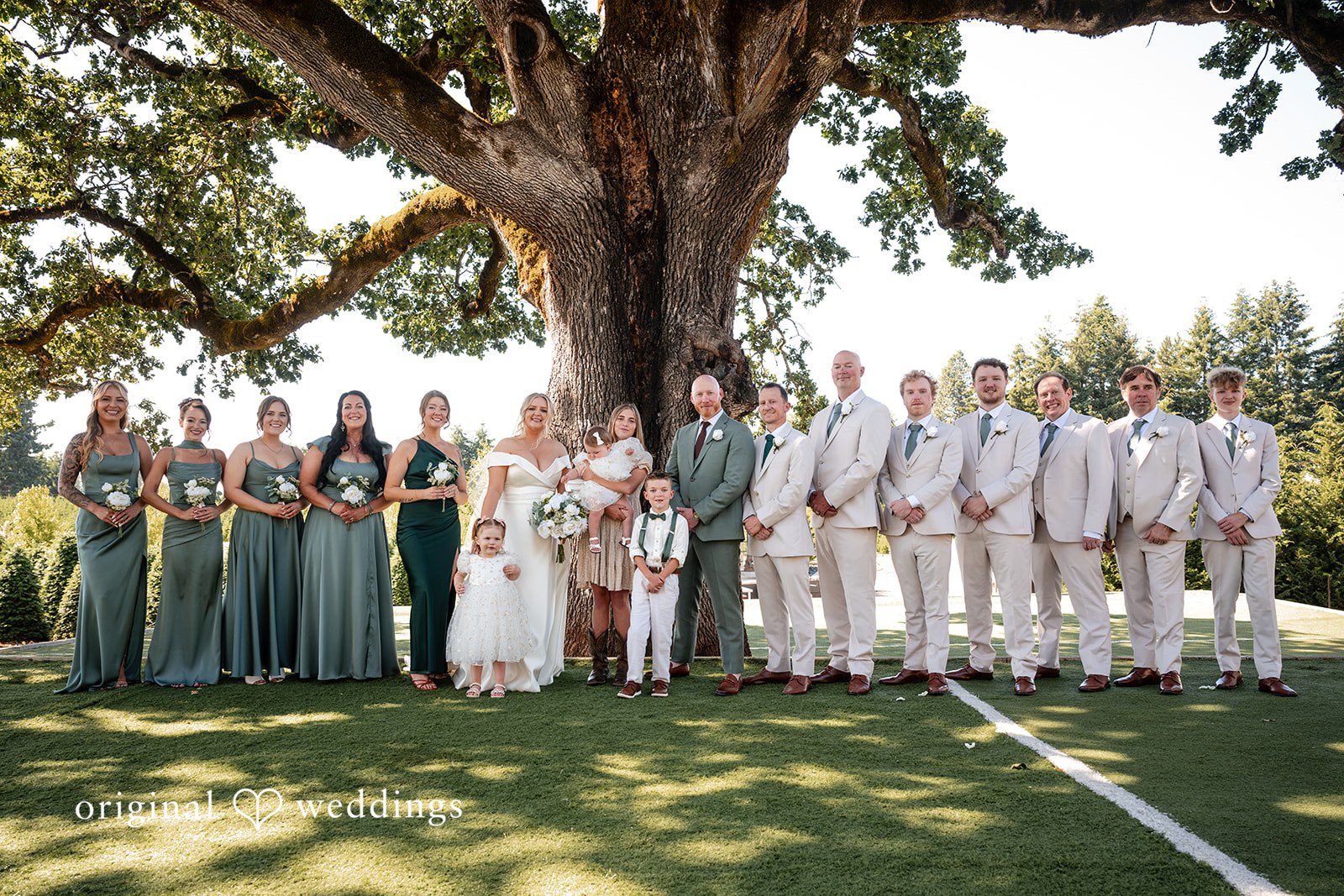 Victoria + Skyler Large wedding party posing together for a group photo under a tree.