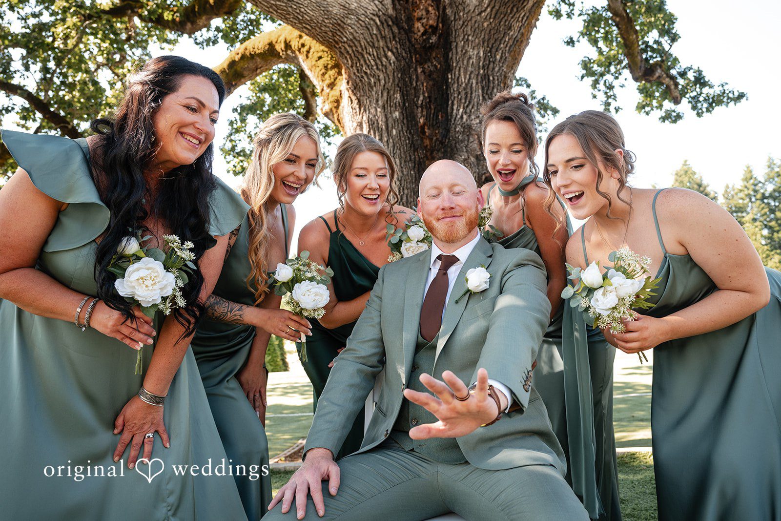 Victoria + Skyler Groom laughing while seated in front of bridesmaids in green dresses.