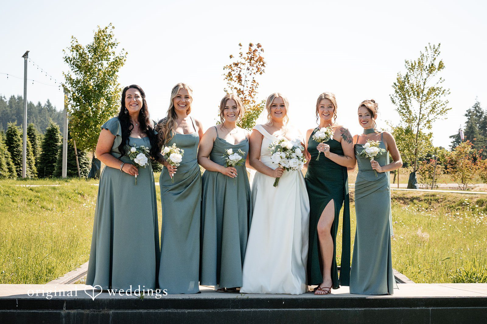 Victoria + Skyler Bride and bridesmaids wearing matching sage green dresses standing in a row.