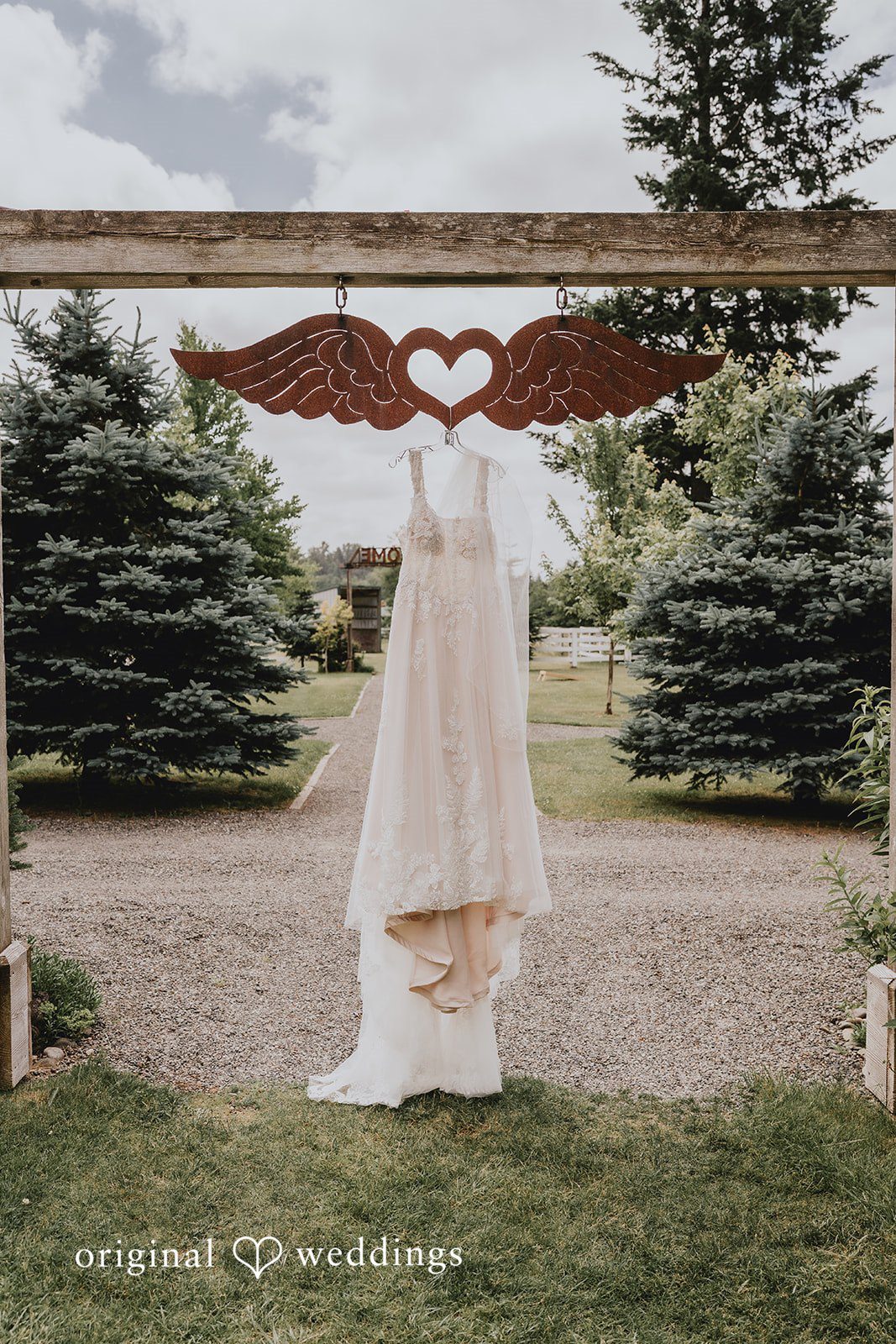 Natalie + DJ Lovely white wedding gown hang across a beautiful hanger with wings at Rein Fire Ranch