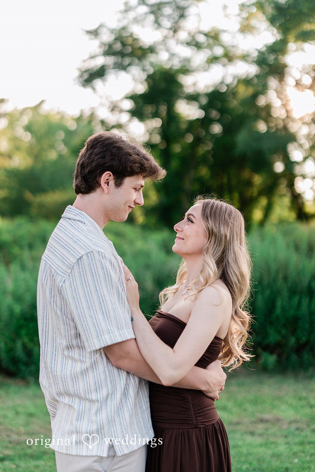 Sara + Jack A couple facing each other and smiling affectionately in a grassy field.