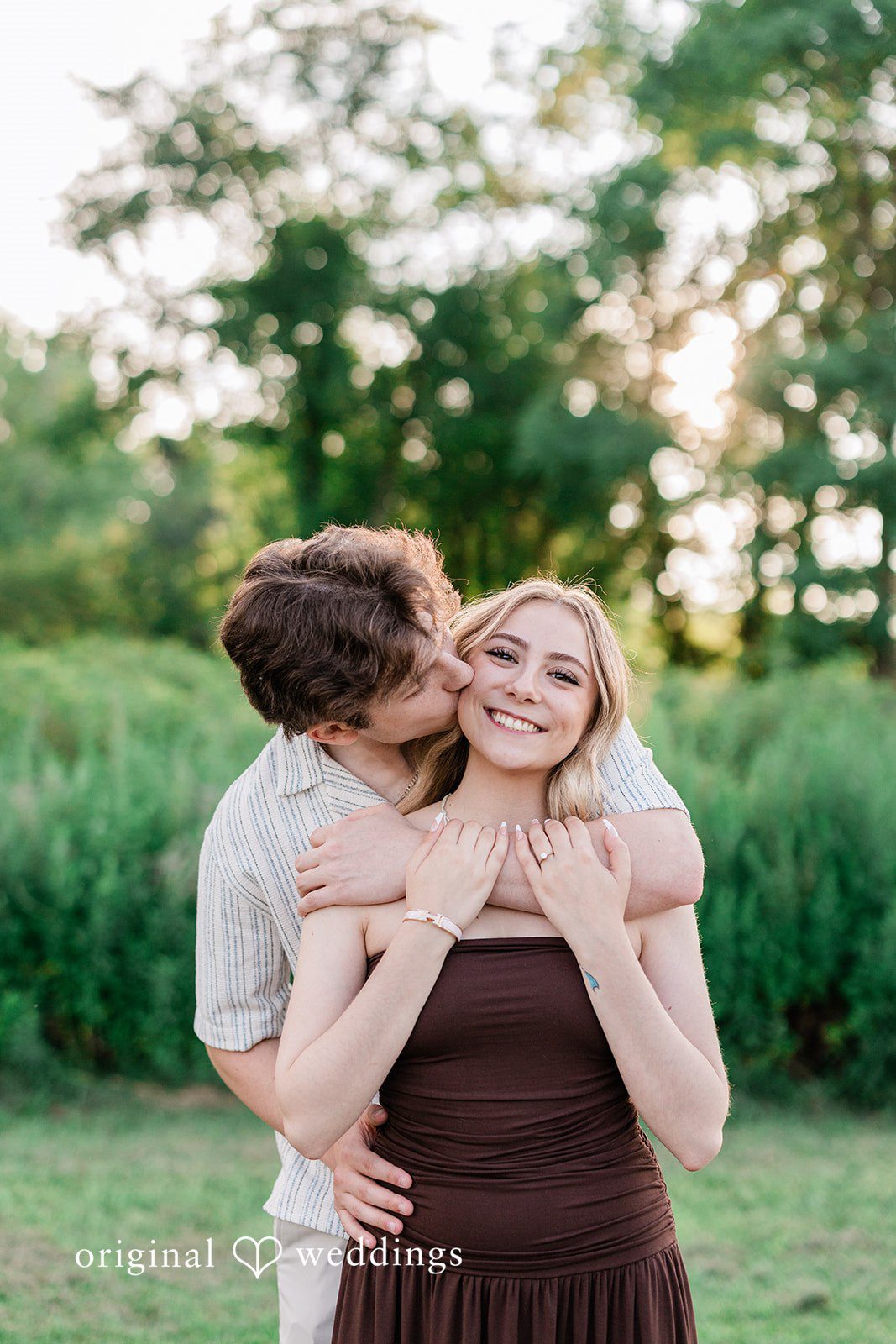 Sara + Jack A wide shot of a couple playfully posing far apart near a rustic red building.