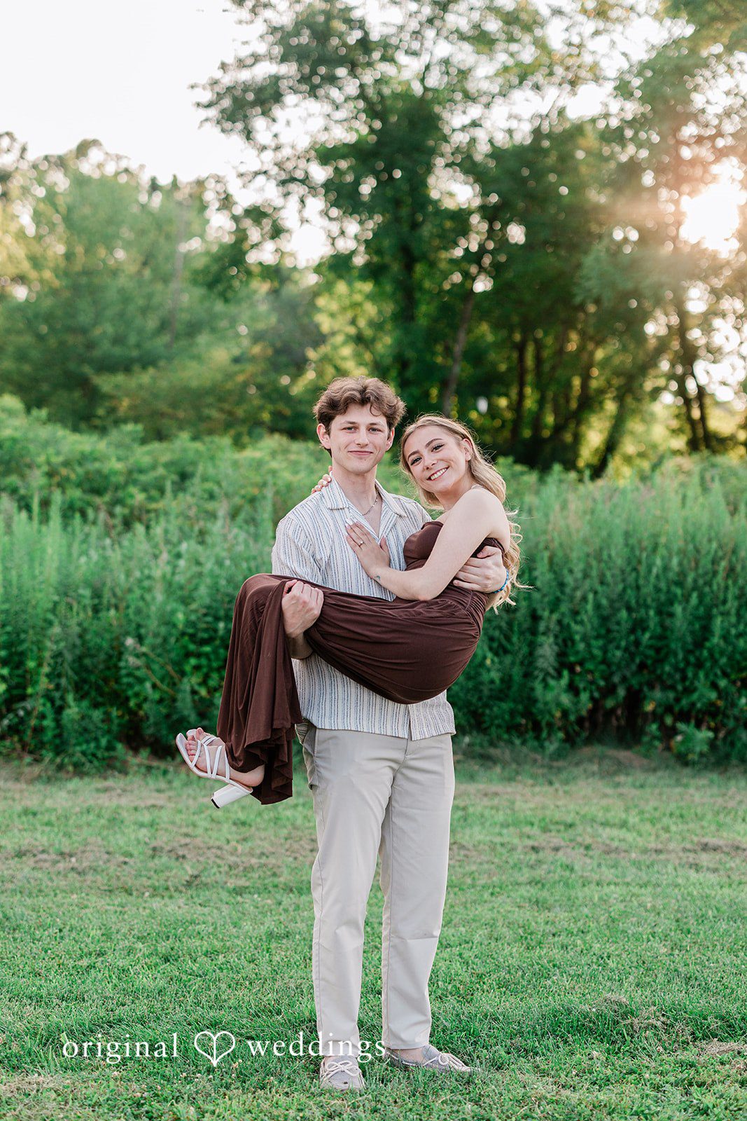 Sara + Jack A man lifting a woman up in his arms while walking through a grassy field.