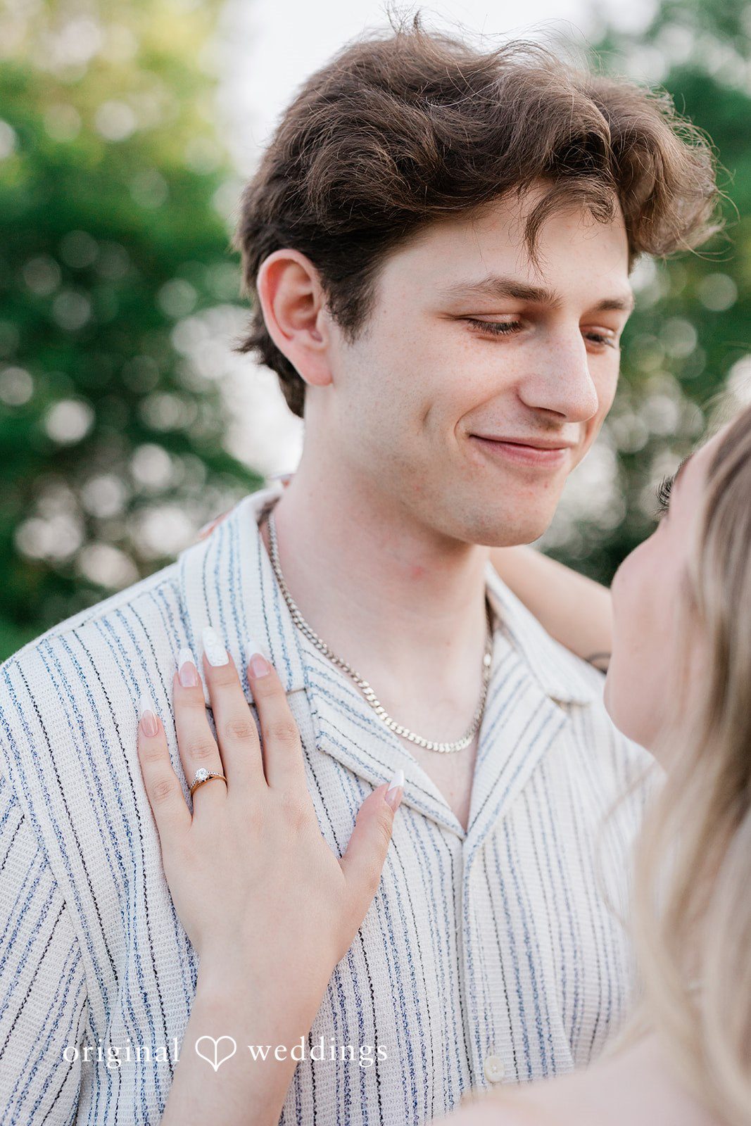Sara + Jack A man in a light-colored button-up shirt smiling warmly as a woman's hand rests on his shoulder.