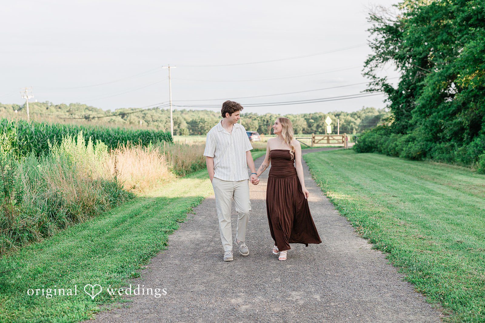 Sara + Jack A couple walking side by side down a long gravel pathway surrounded by tall grass.