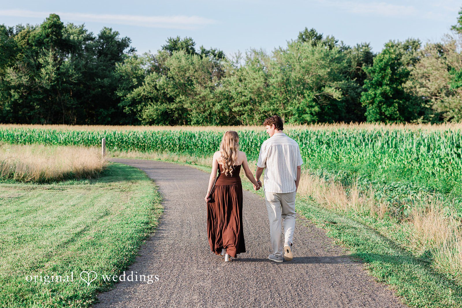 Sara + Jack A couple holding hands walks away down a path next to a field.