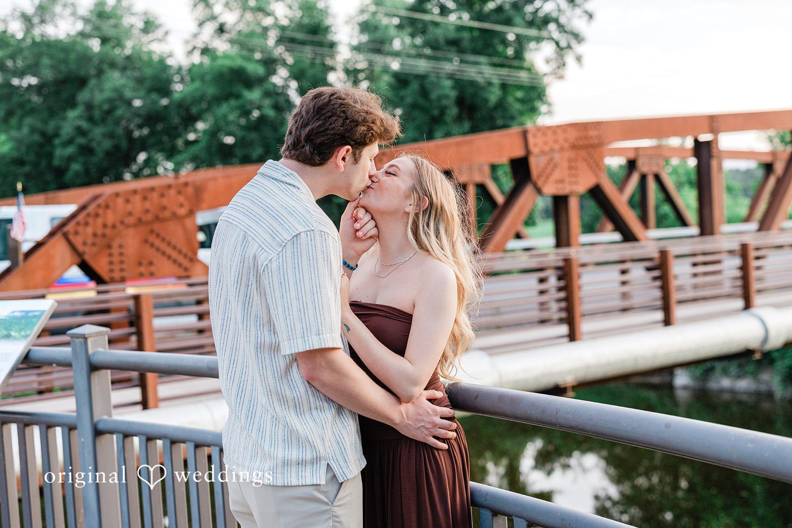 Sara + Jack A couple embracing closely on a wooden bridge deck next to a metal railing.
