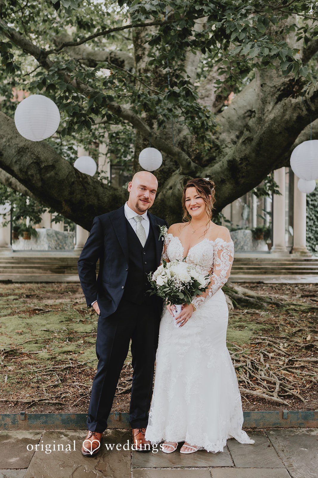 Samantha + Michael Bride and groom holding hands under a large shade tree.