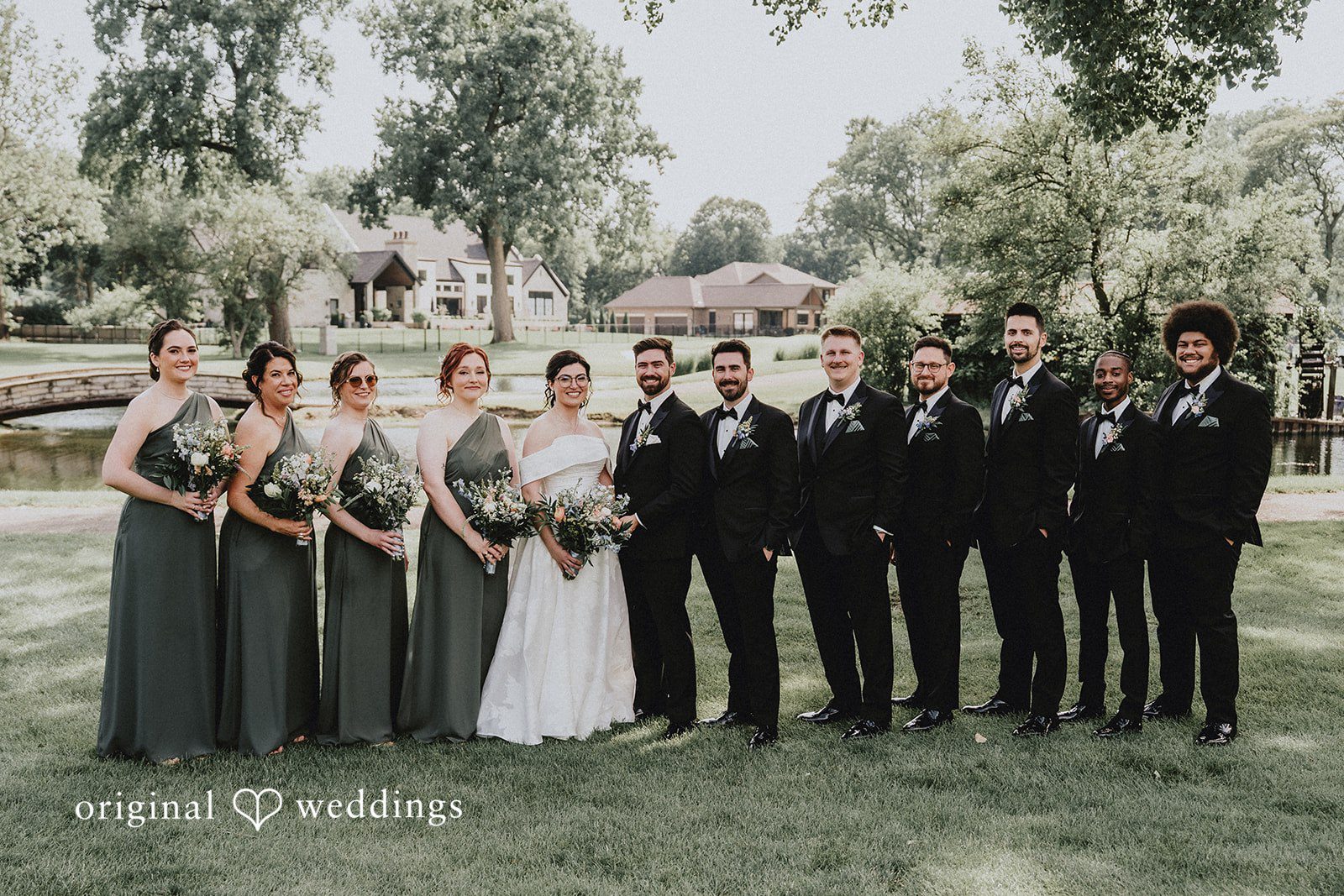 Brandon + Natalie A full wedding party in formal attire posing in a row on a lawn.