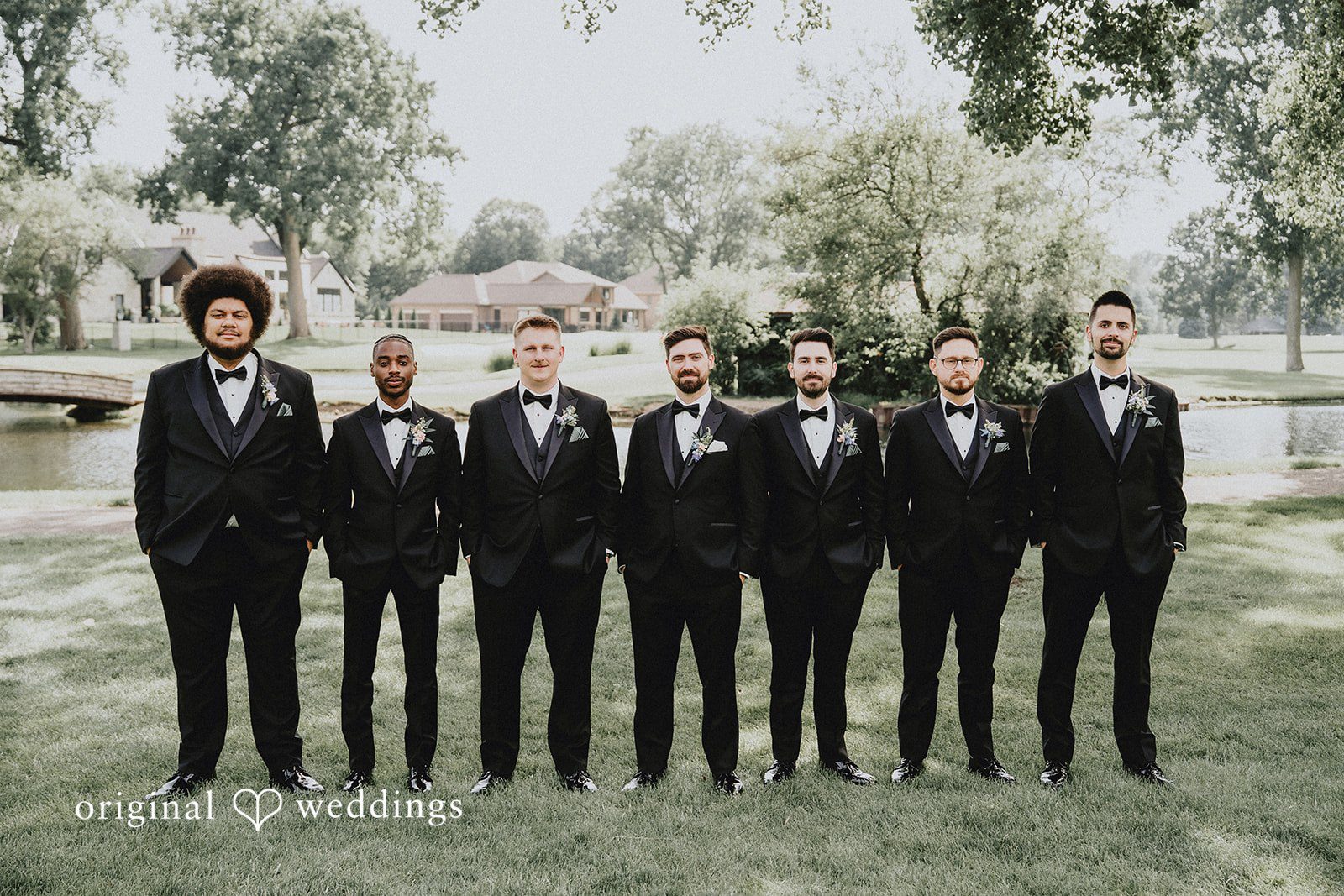 Brandon + Natalie A groom and groomsmen in black suits standing in a row in a park.