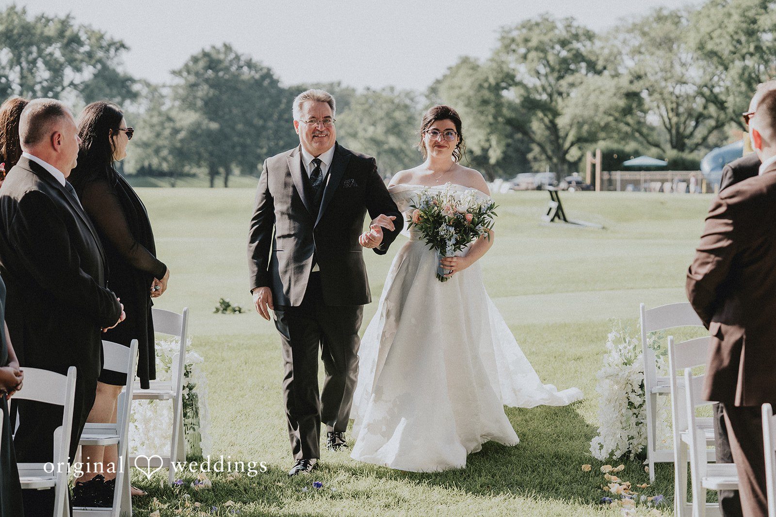 Brandon + Natalie A bride walking down a grassy aisle with a man toward a ceremony setup.