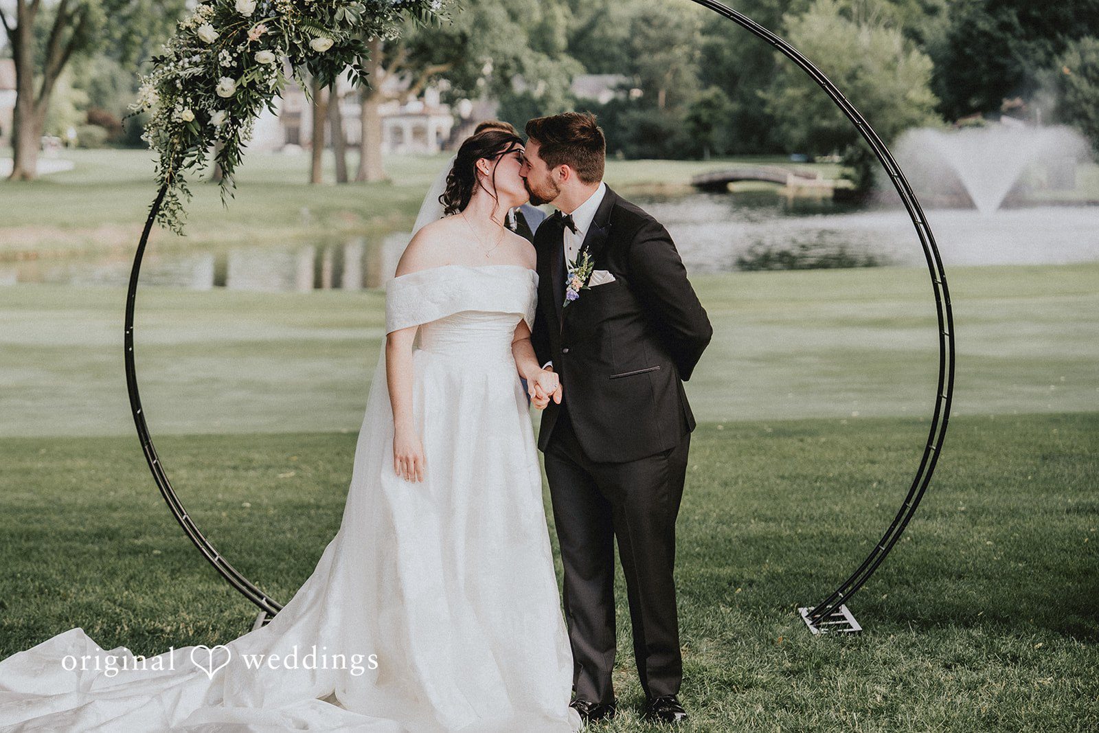 Brandon + Natalie A bride and groom kissing in front of a circular wire wedding arch.