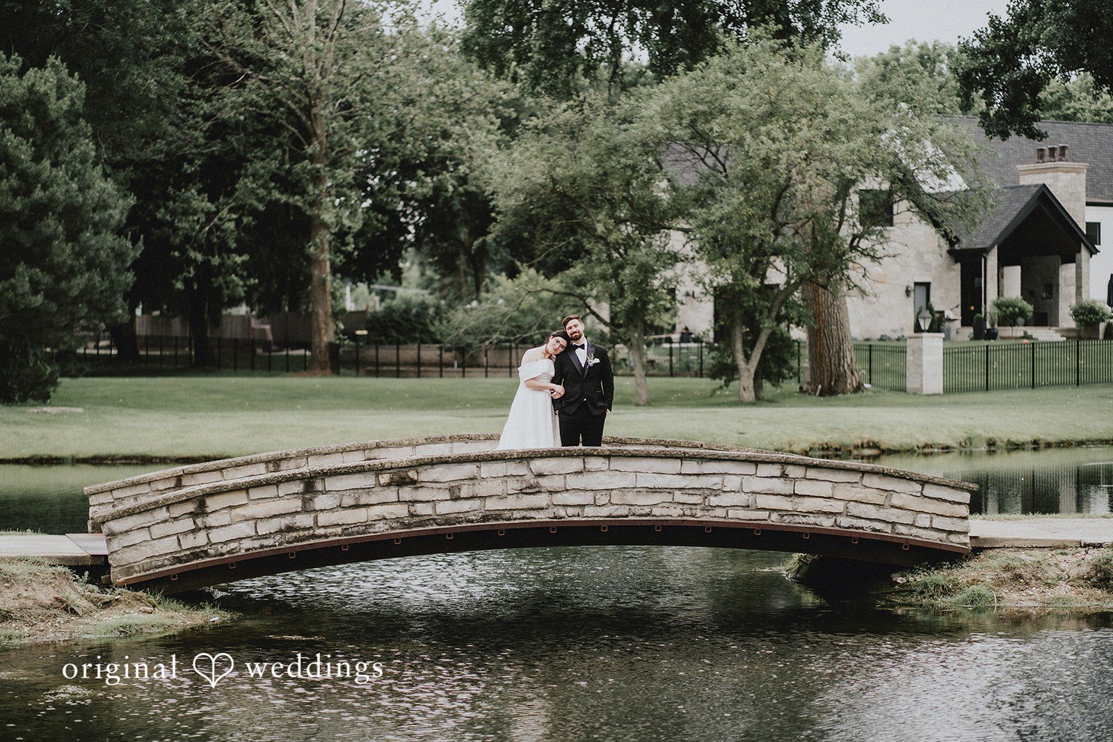Brandon + Natalie A bride and groom standing on a small stone footbridge over water.