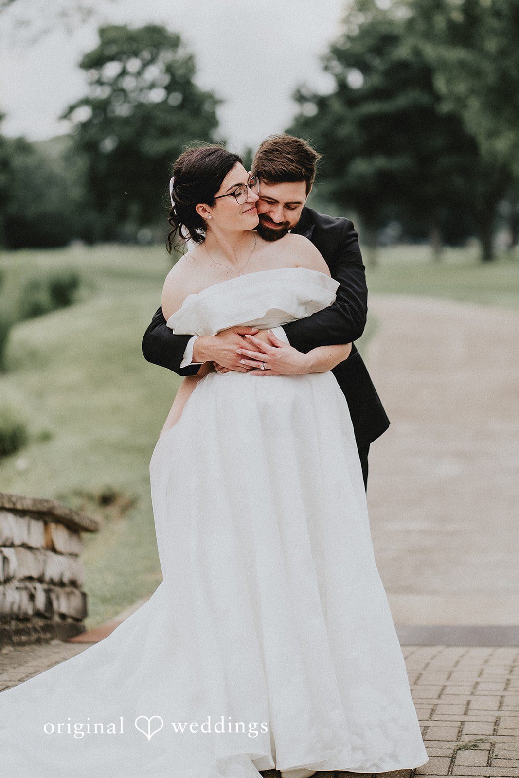 Brandon + Natalie A groom embracing a bride from behind on a paved path.