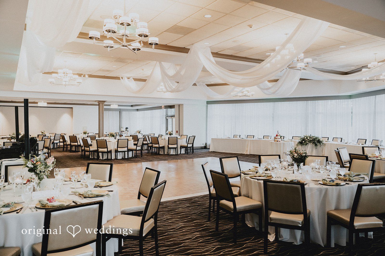 Brandon + Natalie Empty reception tables with white linens and wooden chairs arranged for an event.