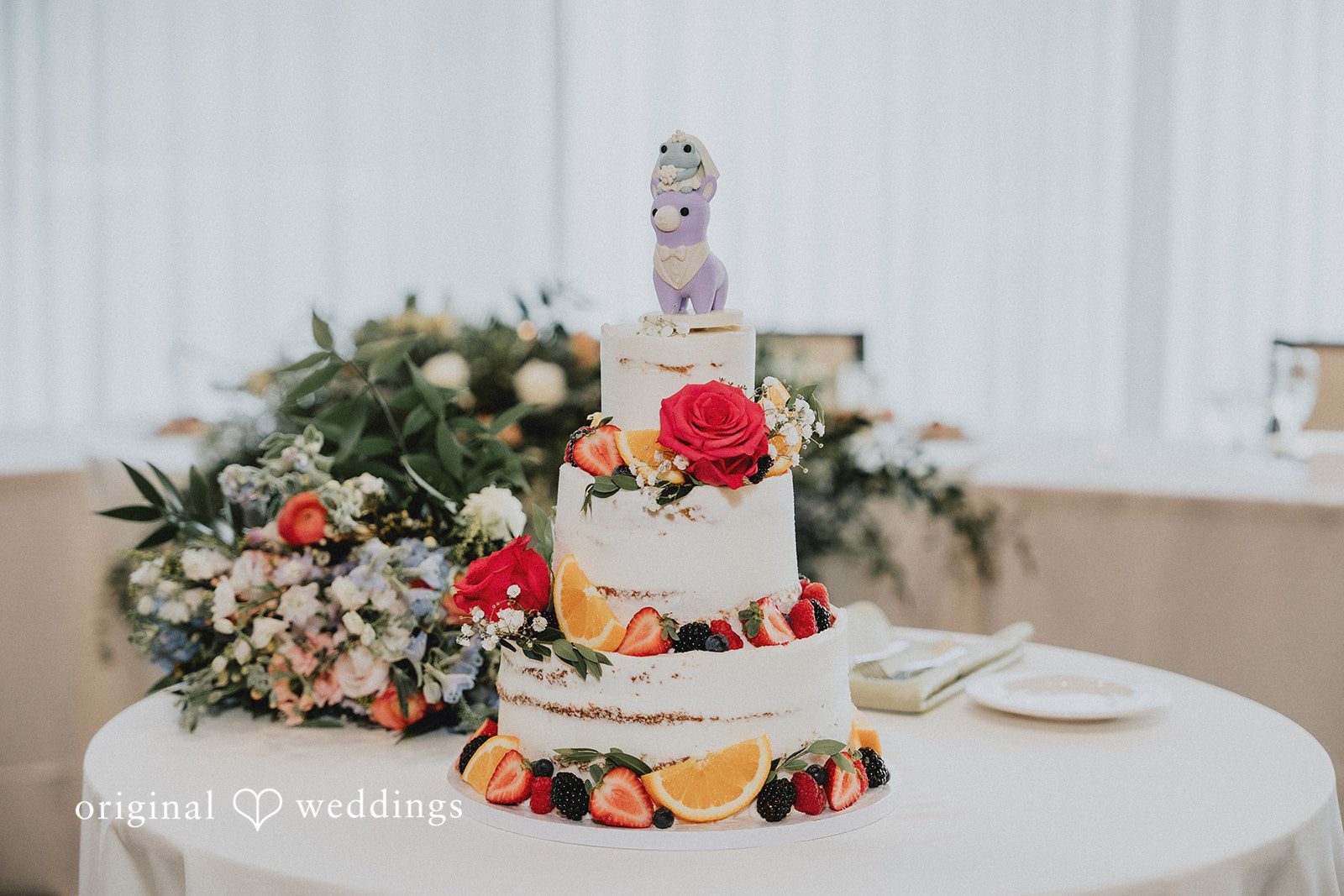 Brandon + Natalie A three-tiered white wedding cake decorated with colorful flowers on a table.