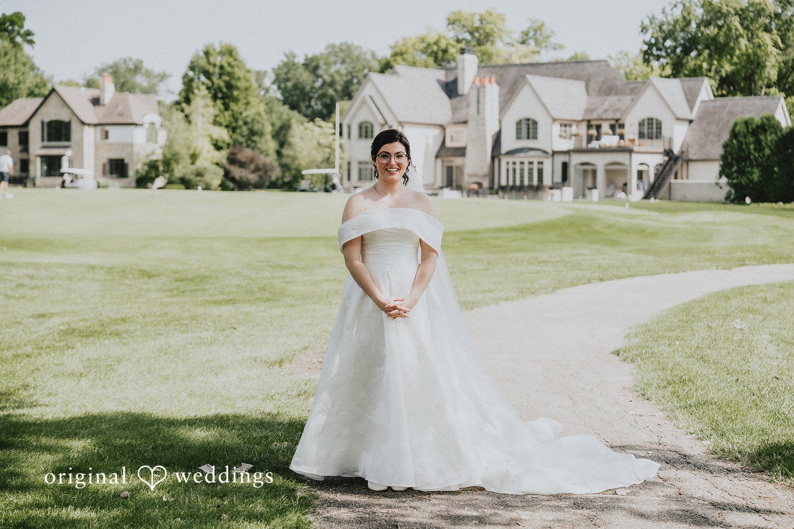 Brandon + Natalie A bride in a long white dress posing on a paved pathway near a lawn.