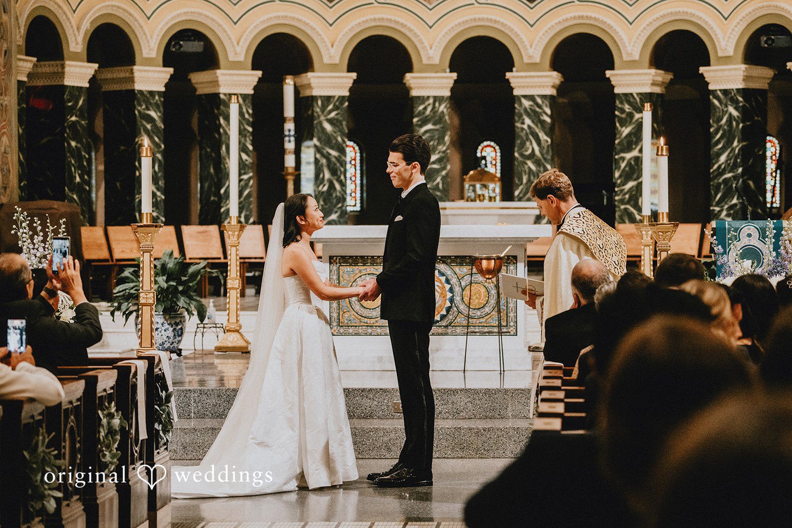 Aleksandar + Anna A bride and groom facing each other at the altar in a church.