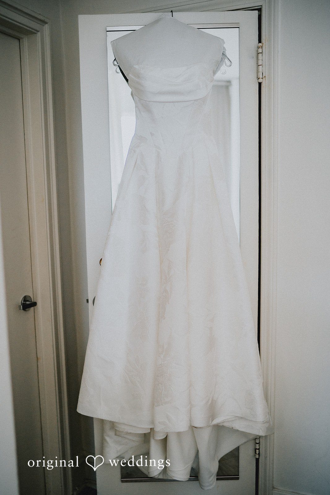Aleksandar + Anna A white bridal gown hanging inside an open doorway.