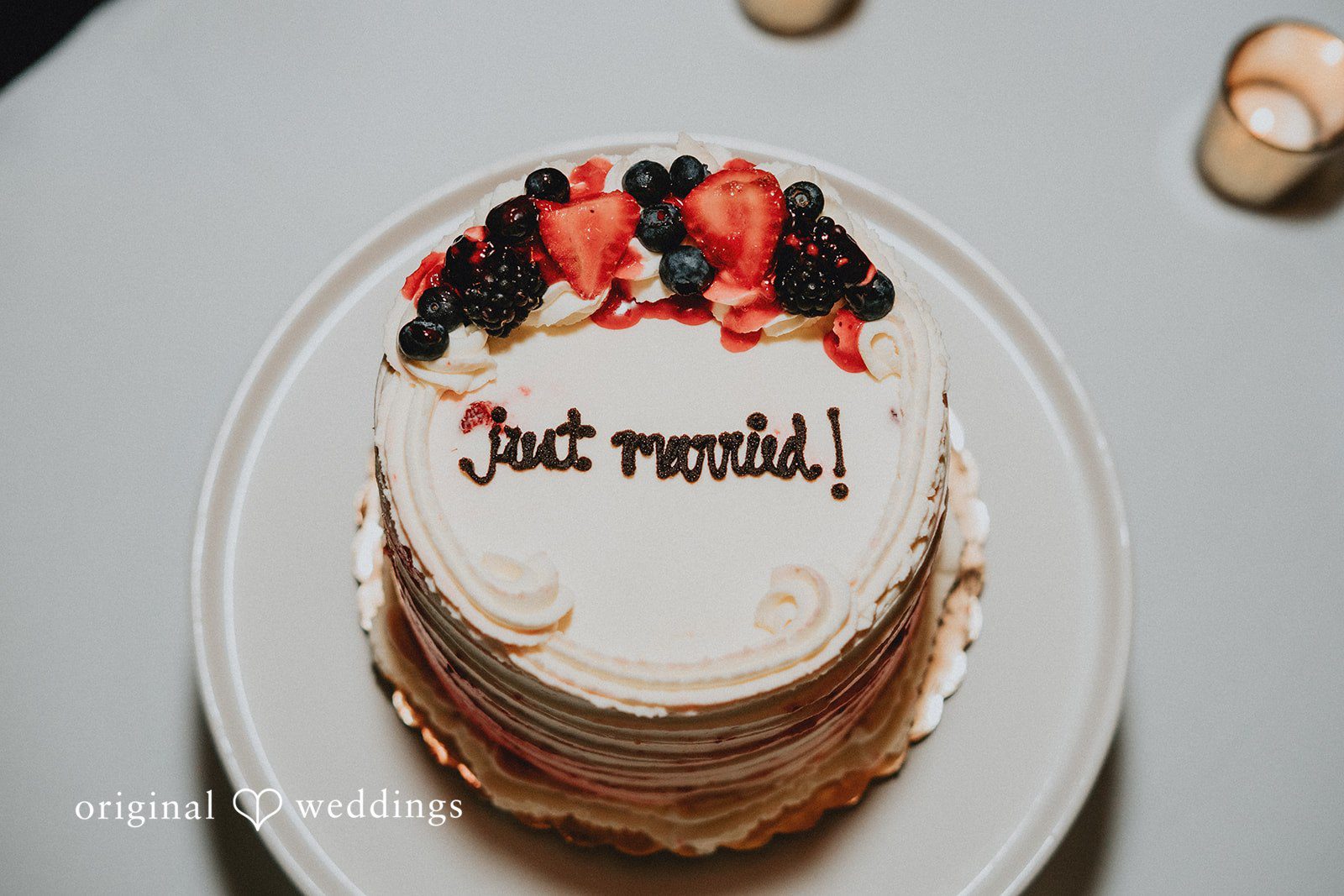 Aleksandar + Anna A white wedding cake topped with fresh berries and chocolate drizzle on a plate.