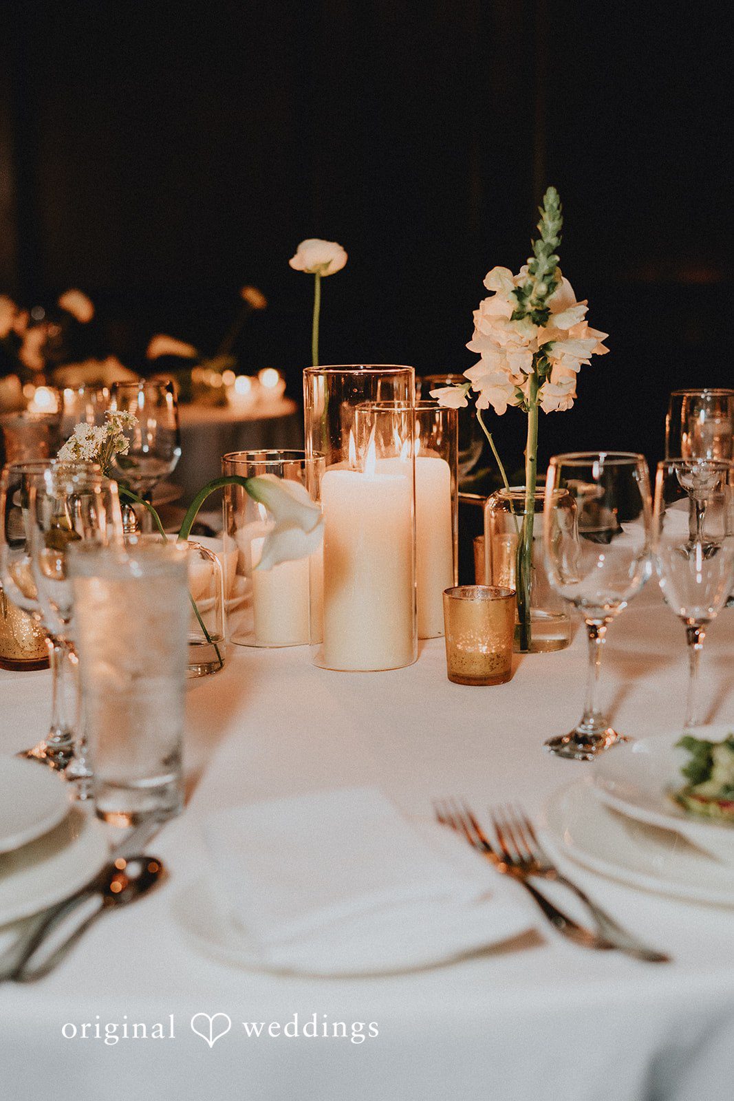 Aleksandar + Anna A close-up of a wedding reception table setting featuring candles and glassware.