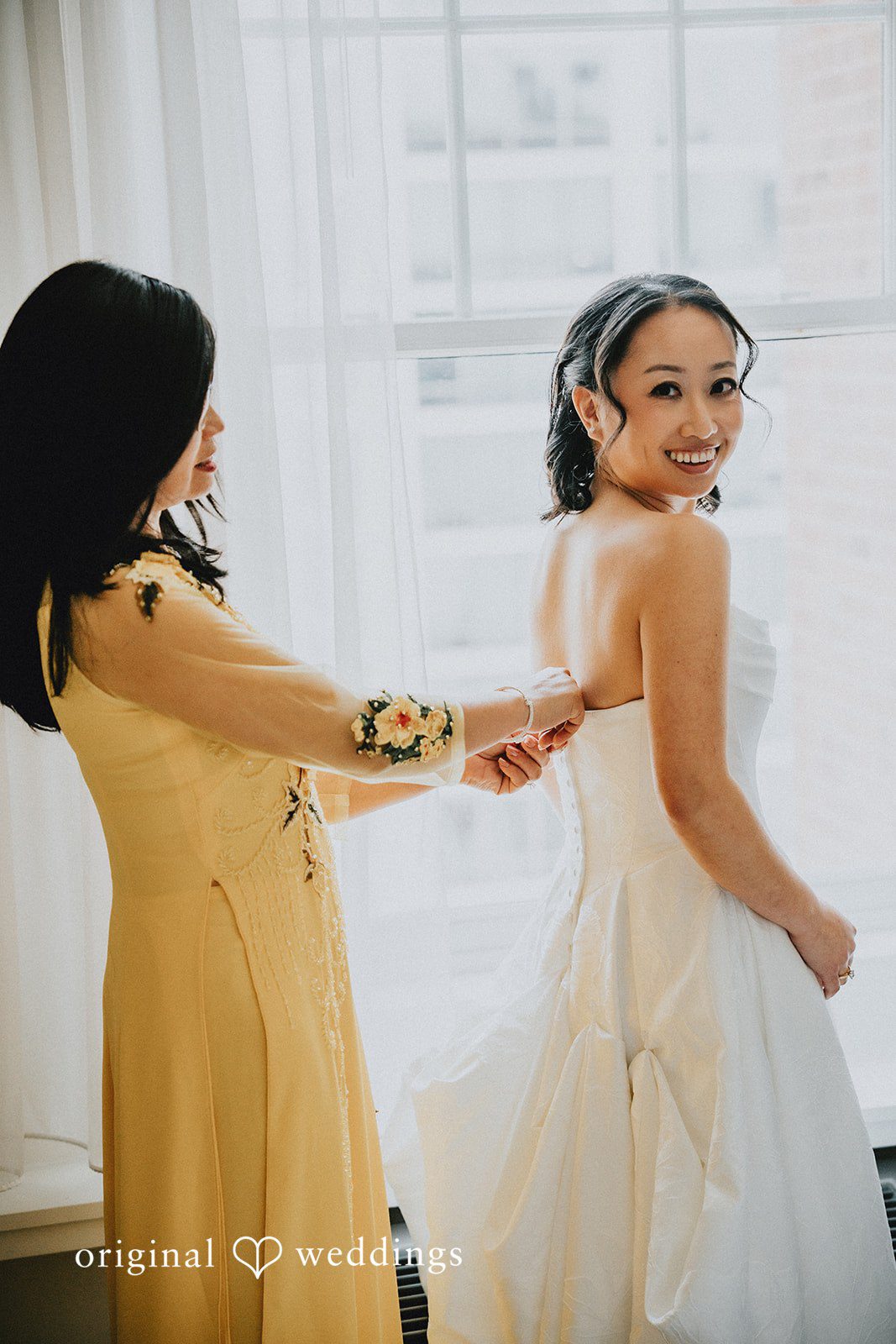 Aleksandar + Anna A bridesmaid assisting a bride with the back of her white wedding dress.