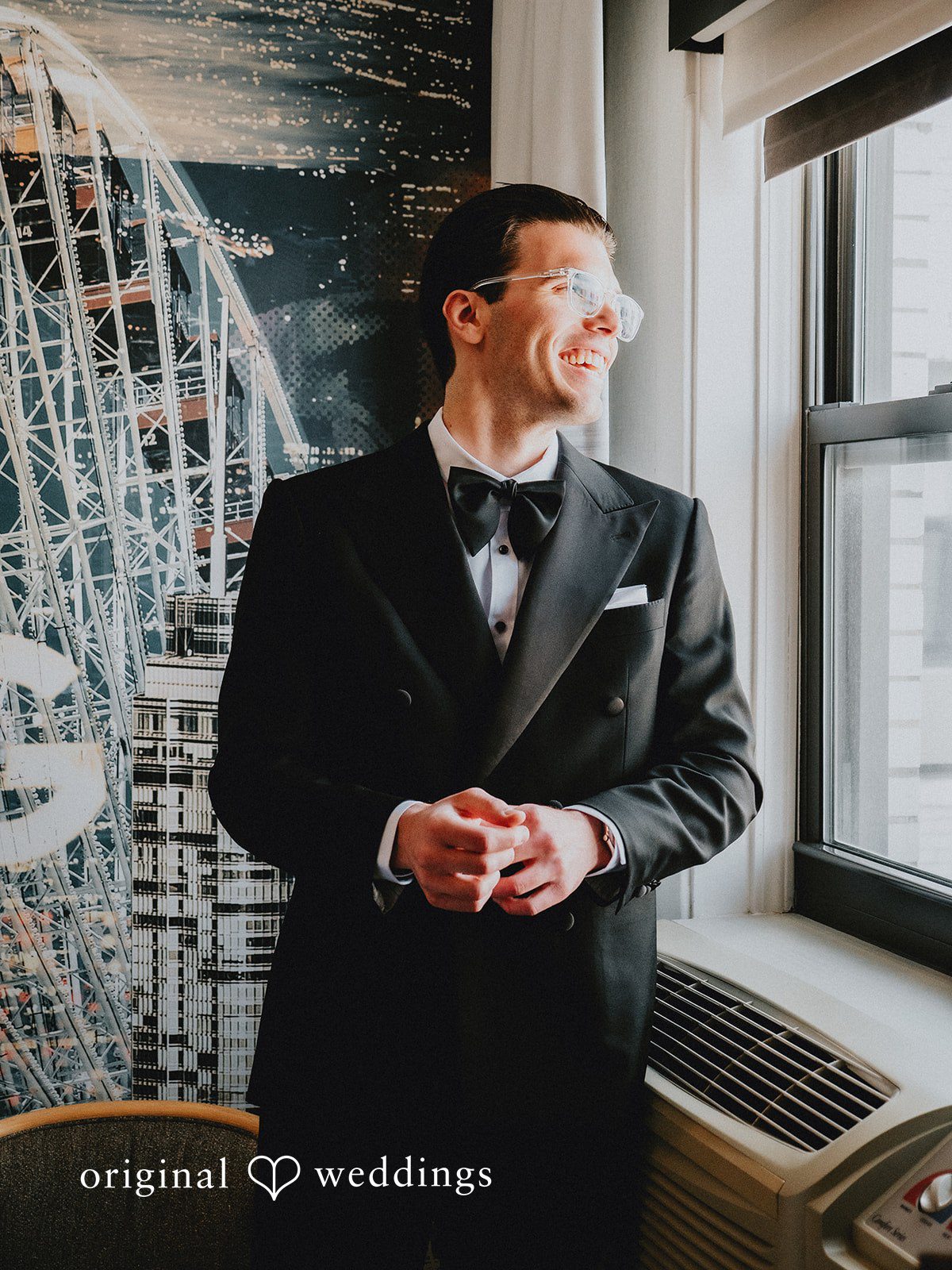 Aleksandar + Anna A groom in a black tuxedo smiling while standing near a window.