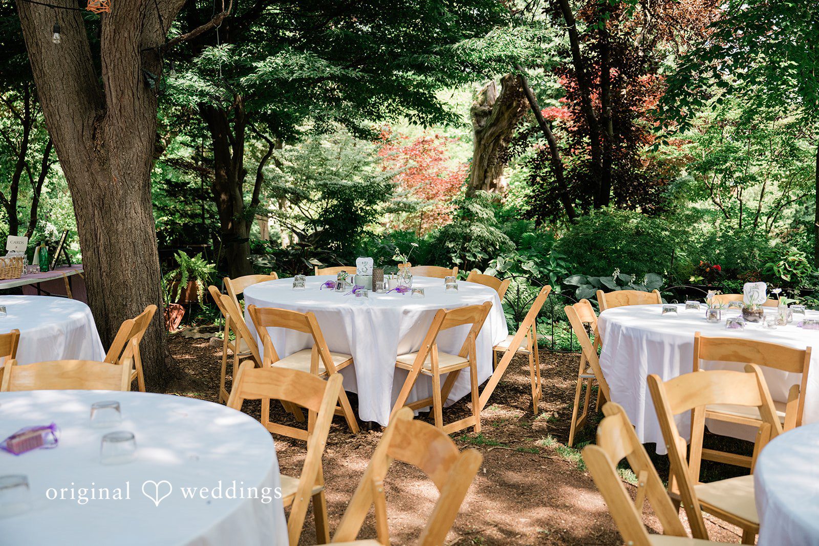 Lauren + Brinton Empty round tables with white tablecloths and wooden chairs arranged for an event.