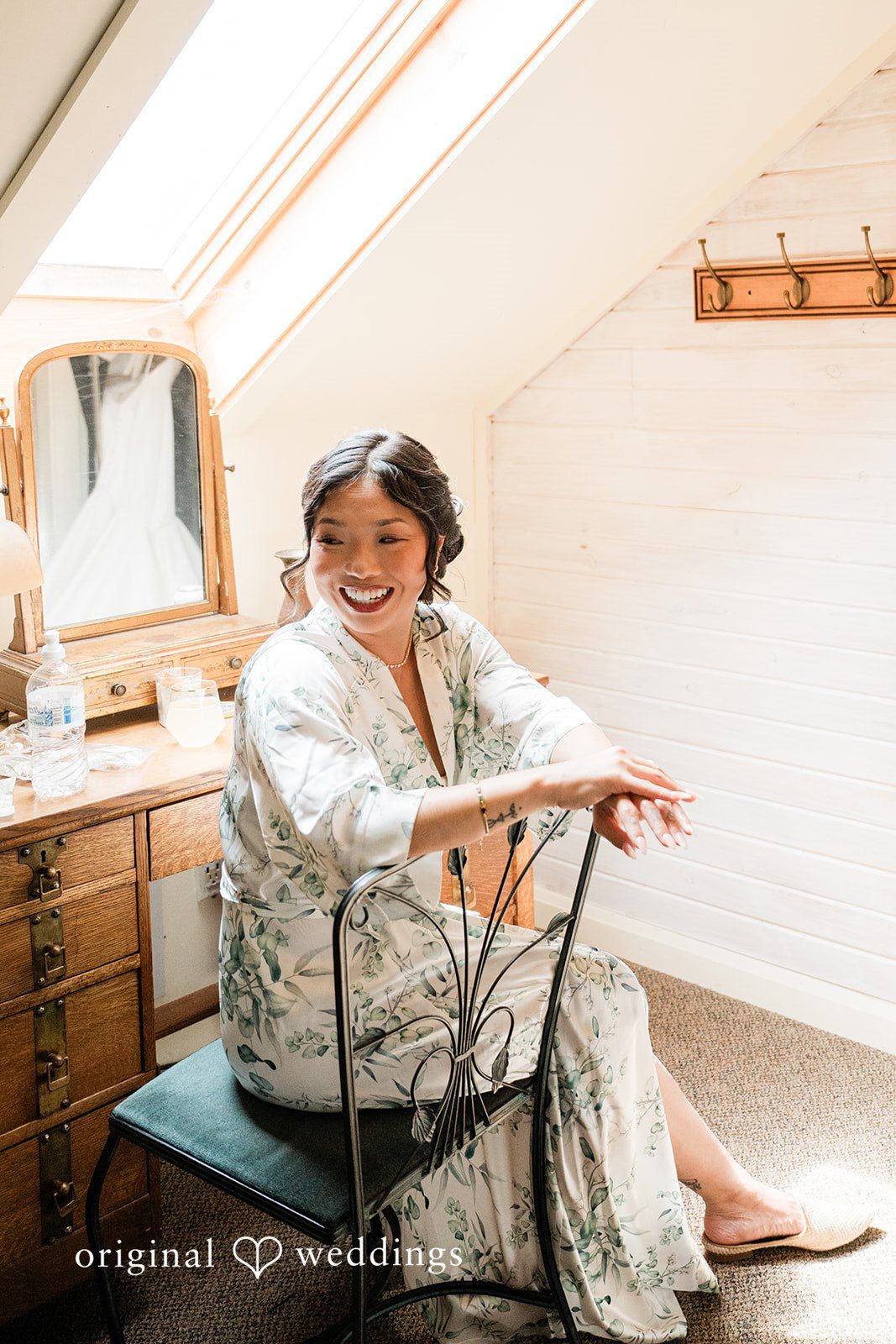 Lauren + Brinton A woman sitting in a white robe while getting ready in a bright room.