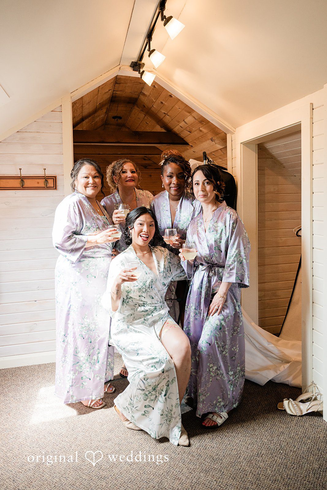 Lauren + Brinton A group of women in robes laughing and celebrating together in a room.