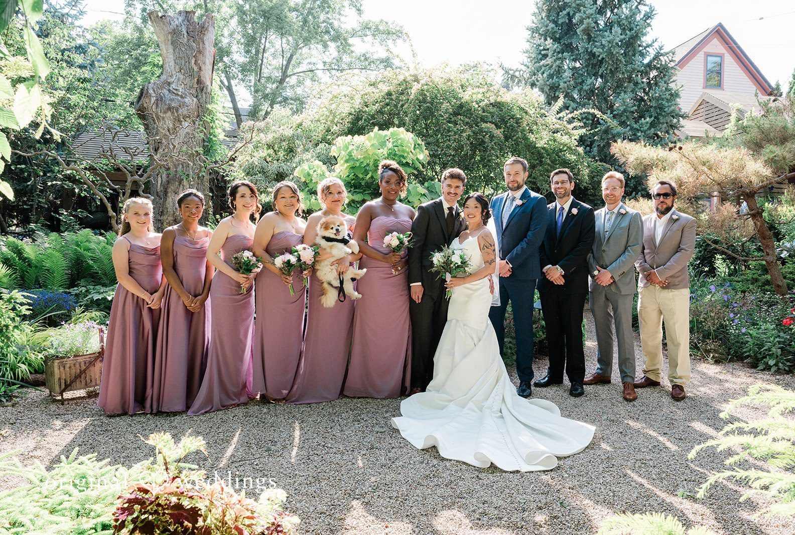 A wedding party in formal wear posing together on a sunny path at Sanger House Gardens by Milwaukee Wedding Photographers from Original Weddings.