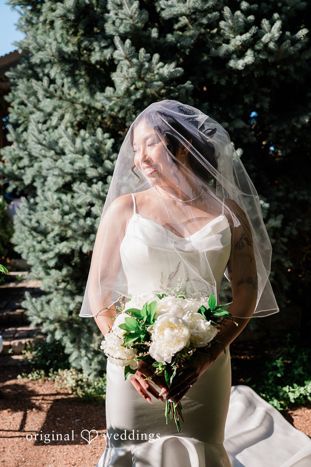 Lauren + Brinton A bride wearing a long sheer veil and holding a white bouquet.