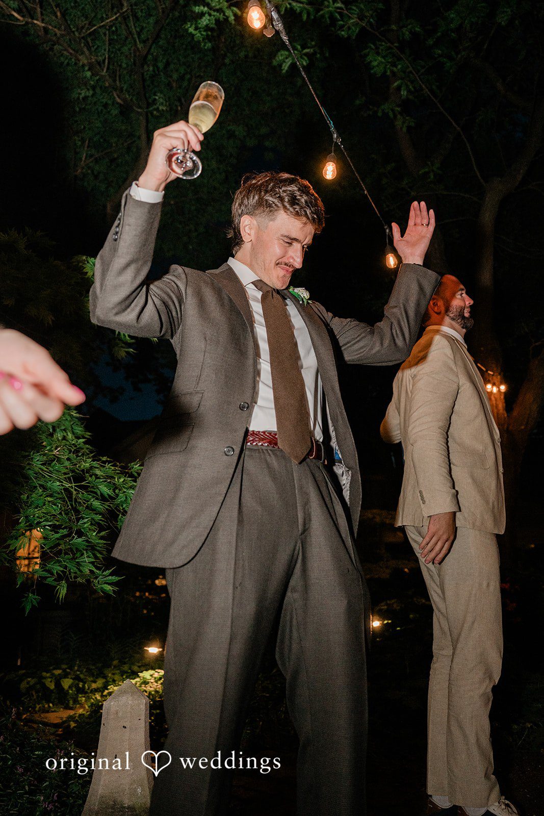 Lauren + Brinton A man in a suit dancing with raised arms at night.