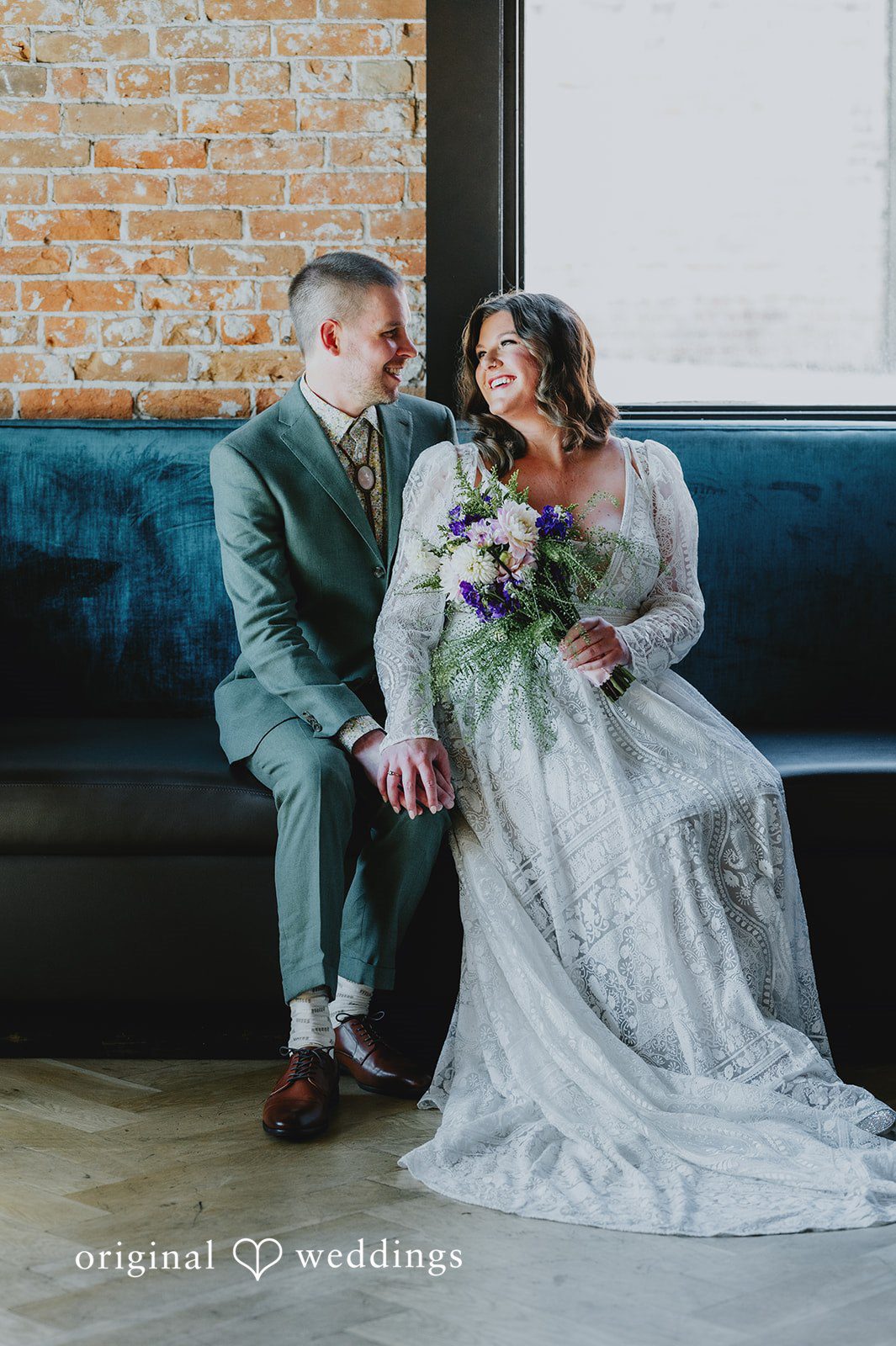 Elizabeth + Willis Couple dressed in wedding attire sitting together on a dark bench.