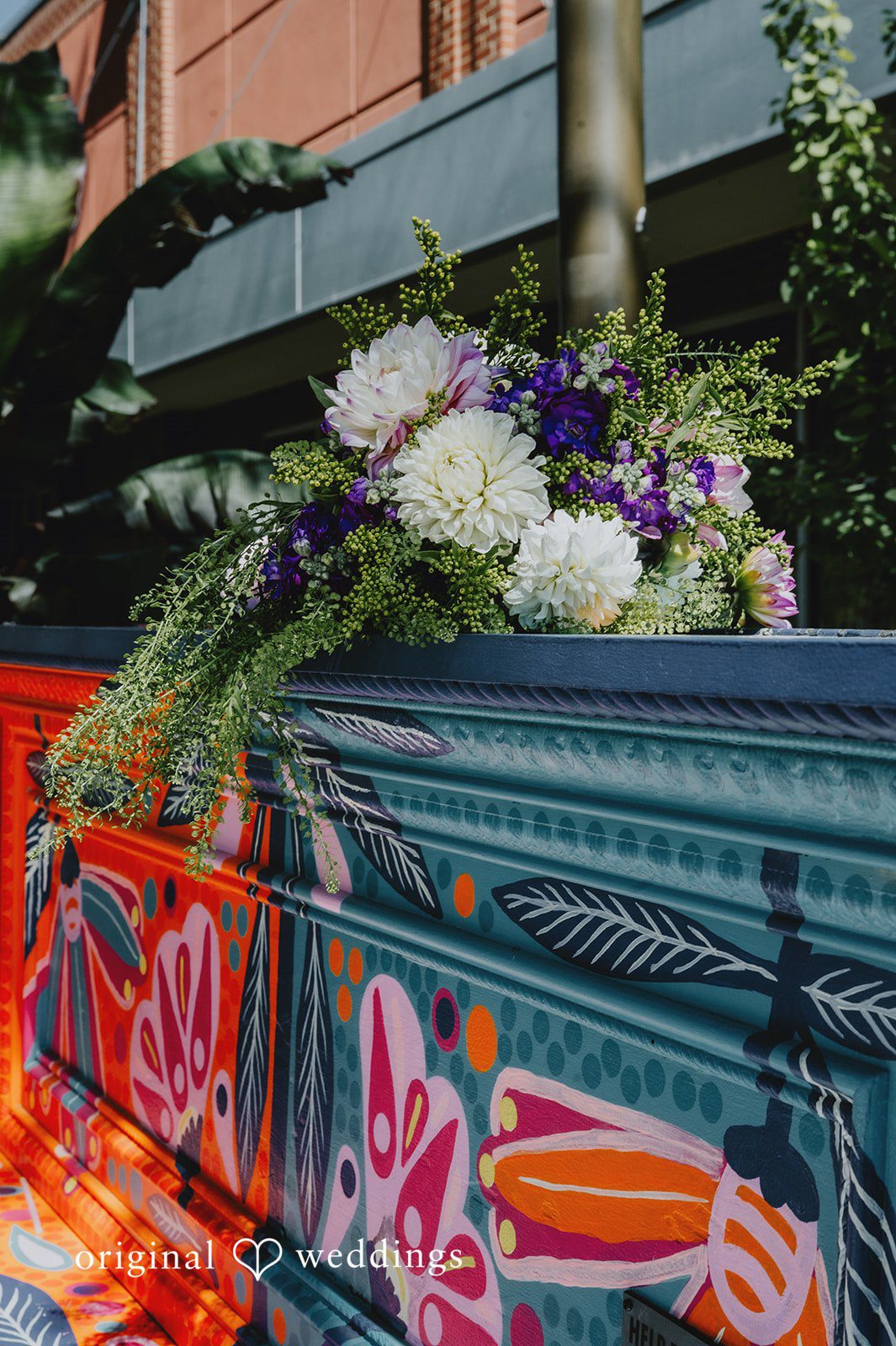 Elizabeth + Willis A vibrant bridal bouquet with white dahlias and purple wildflowers resting on top of a brightly painted piano.
