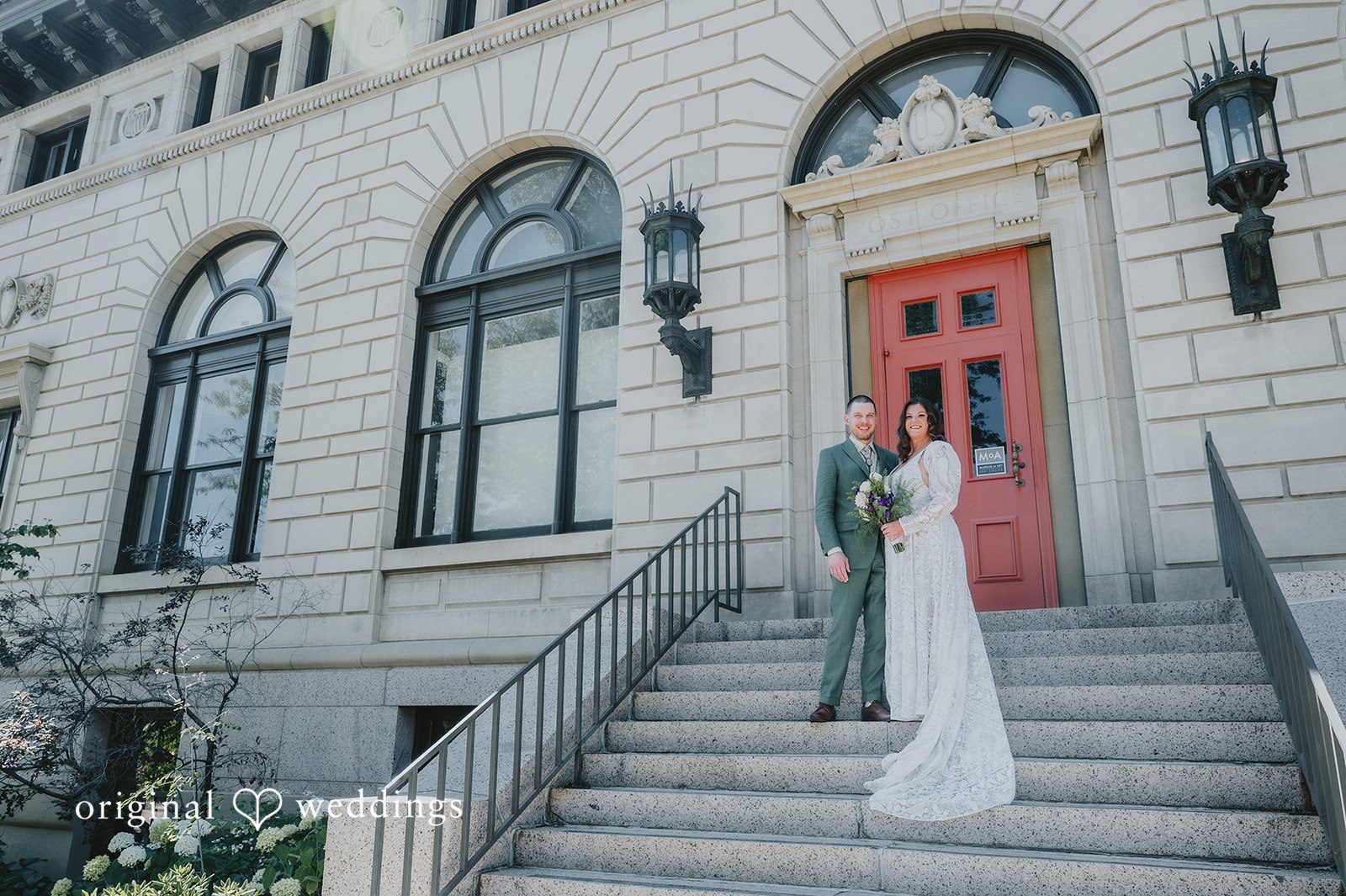 Elizabeth + Willis Bride and groom posing on wide stone steps in front of a building with a large red door.