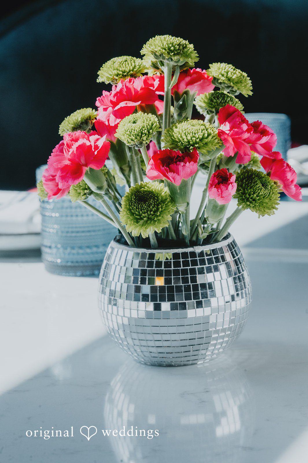 Elizabeth + Willis Vibrant pink flowers arranged inside a reflective disco ball vase on a table.