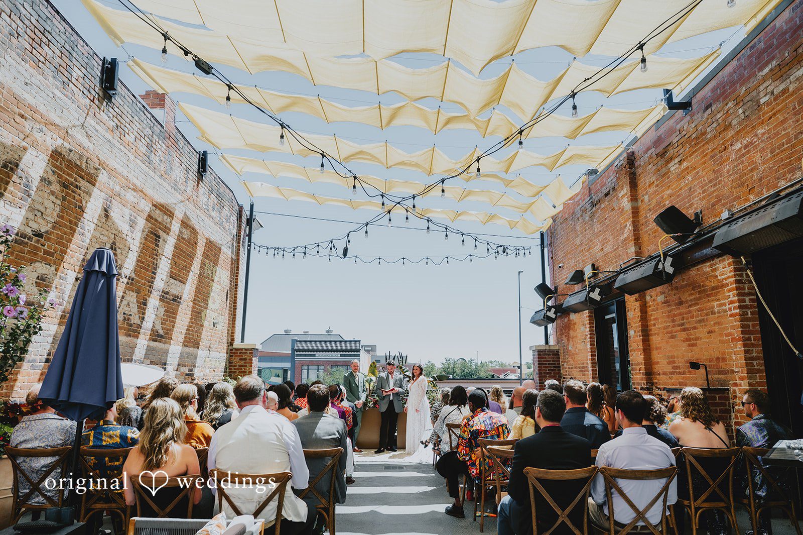Elizabeth + Willis Ceremony aisle under hanging string lights with guests seated on both sides.