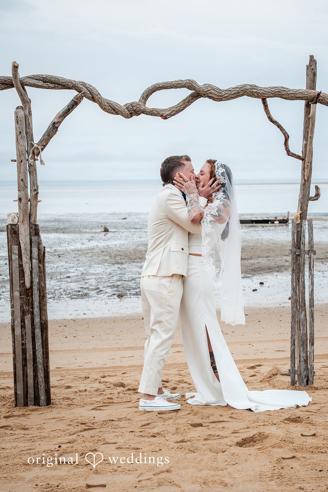 Jacqueline + Sarah A bride and groom sharing a passionate embrace and kiss on the beach.