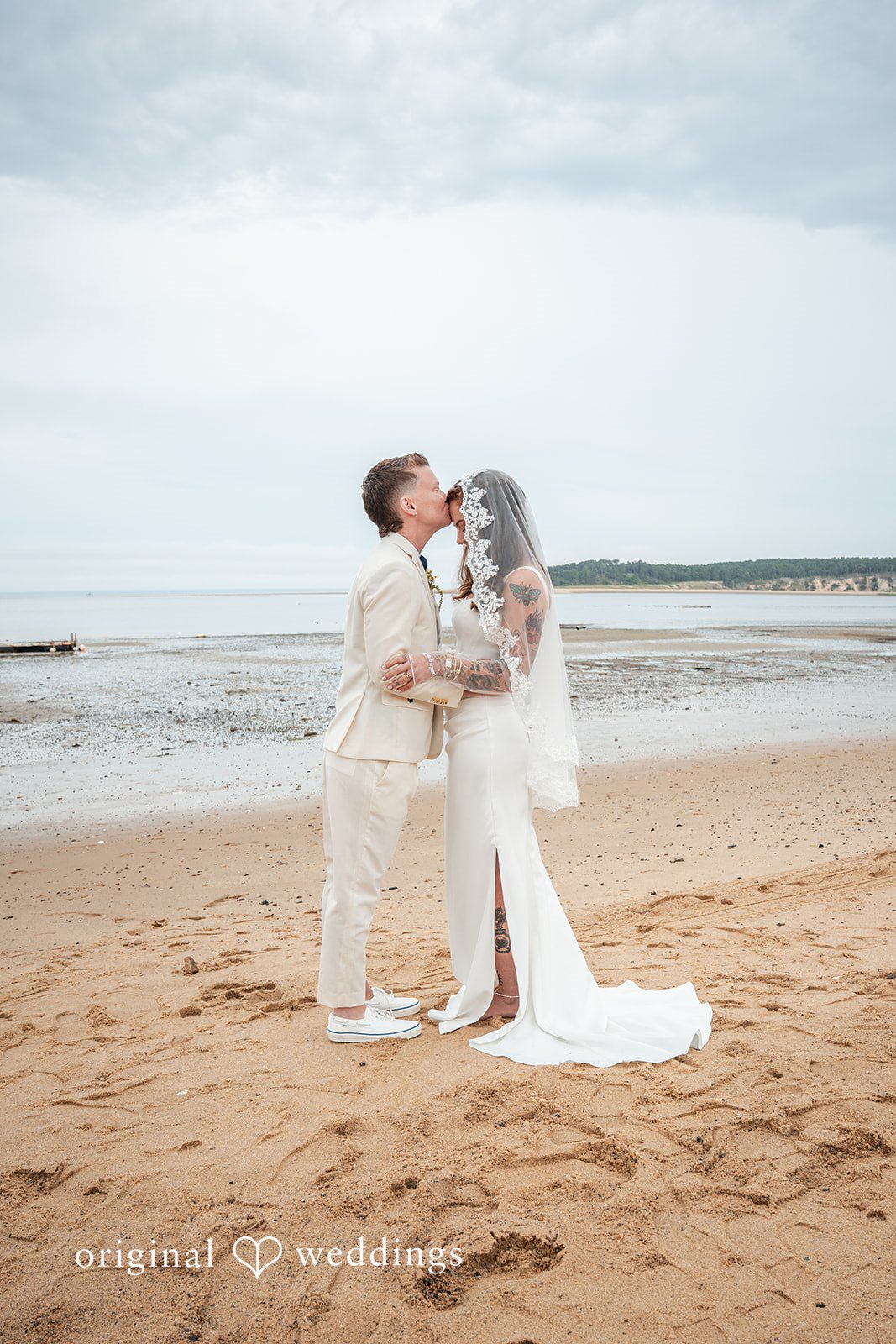 Jacqueline + Sarah A bride and groom sharing a passionate embrace and kiss on the beach.