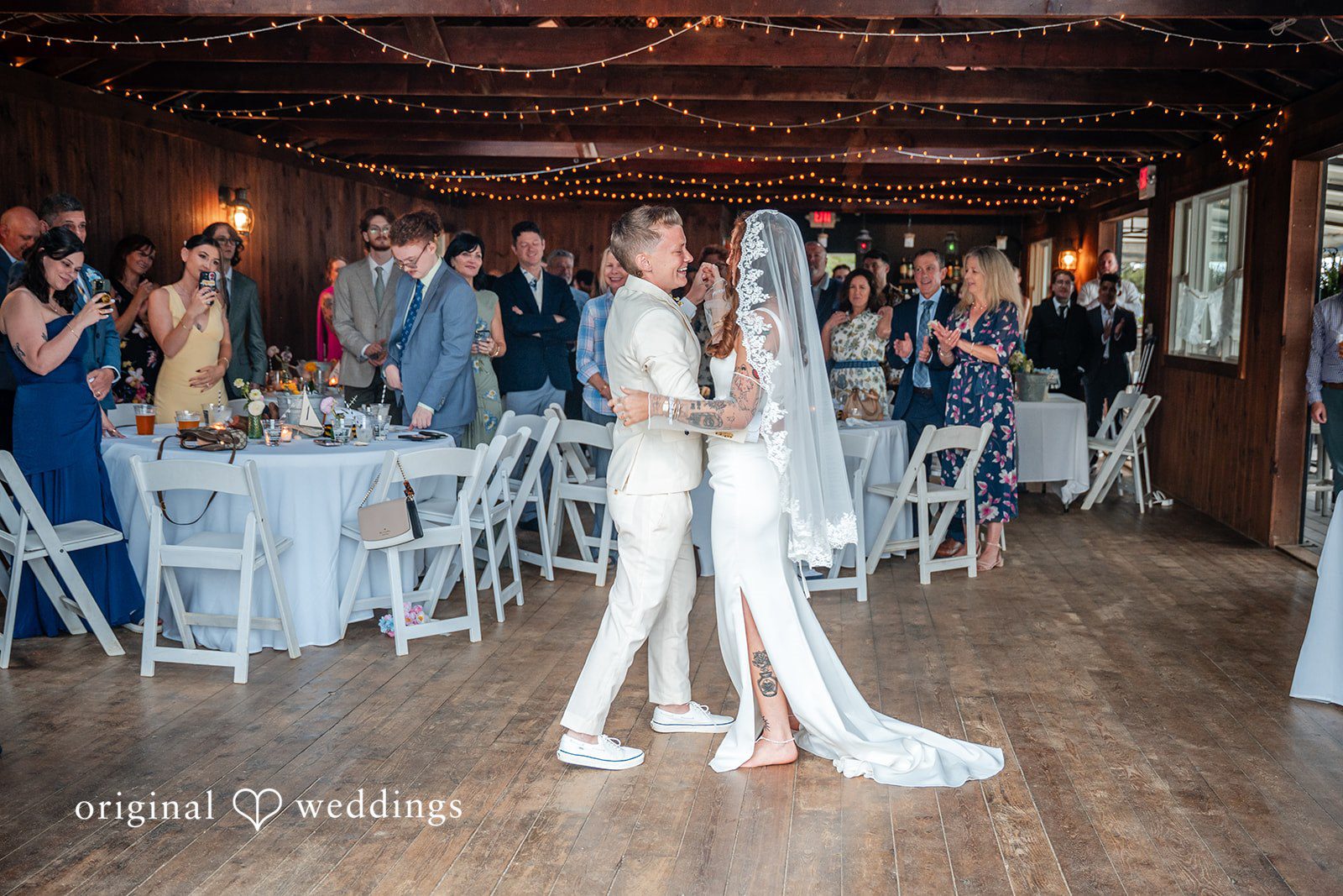 Jacqueline + Sarah A wedding couple sharing a dance surrounded by tables at their reception.