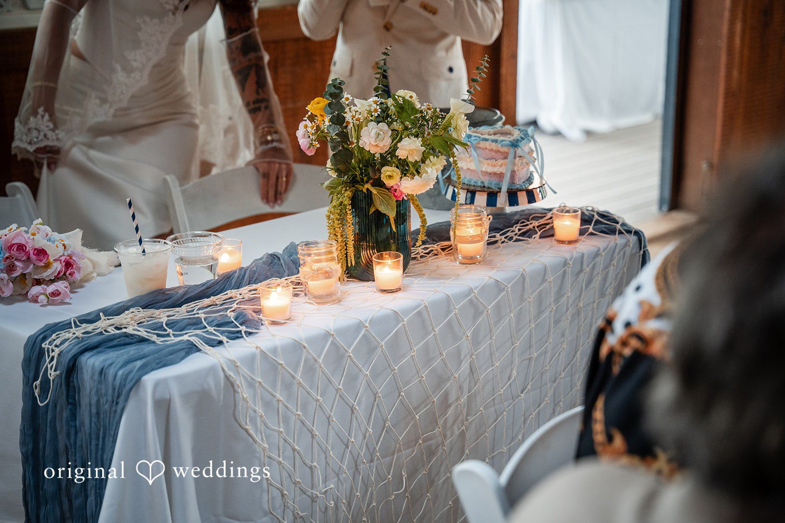 Jacqueline + Sarah A decorated long dinner table lit with candles and lined with blue fabric runner.